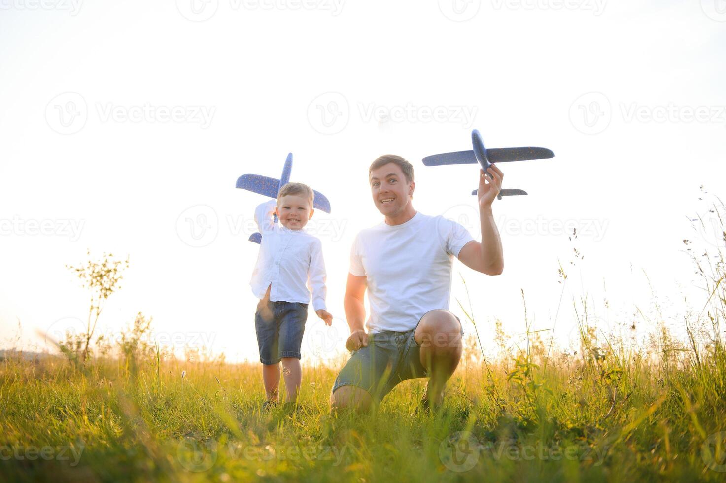 Cute little boy and his handsome young dad are smiling while playing with a toy airplane in the park. photo