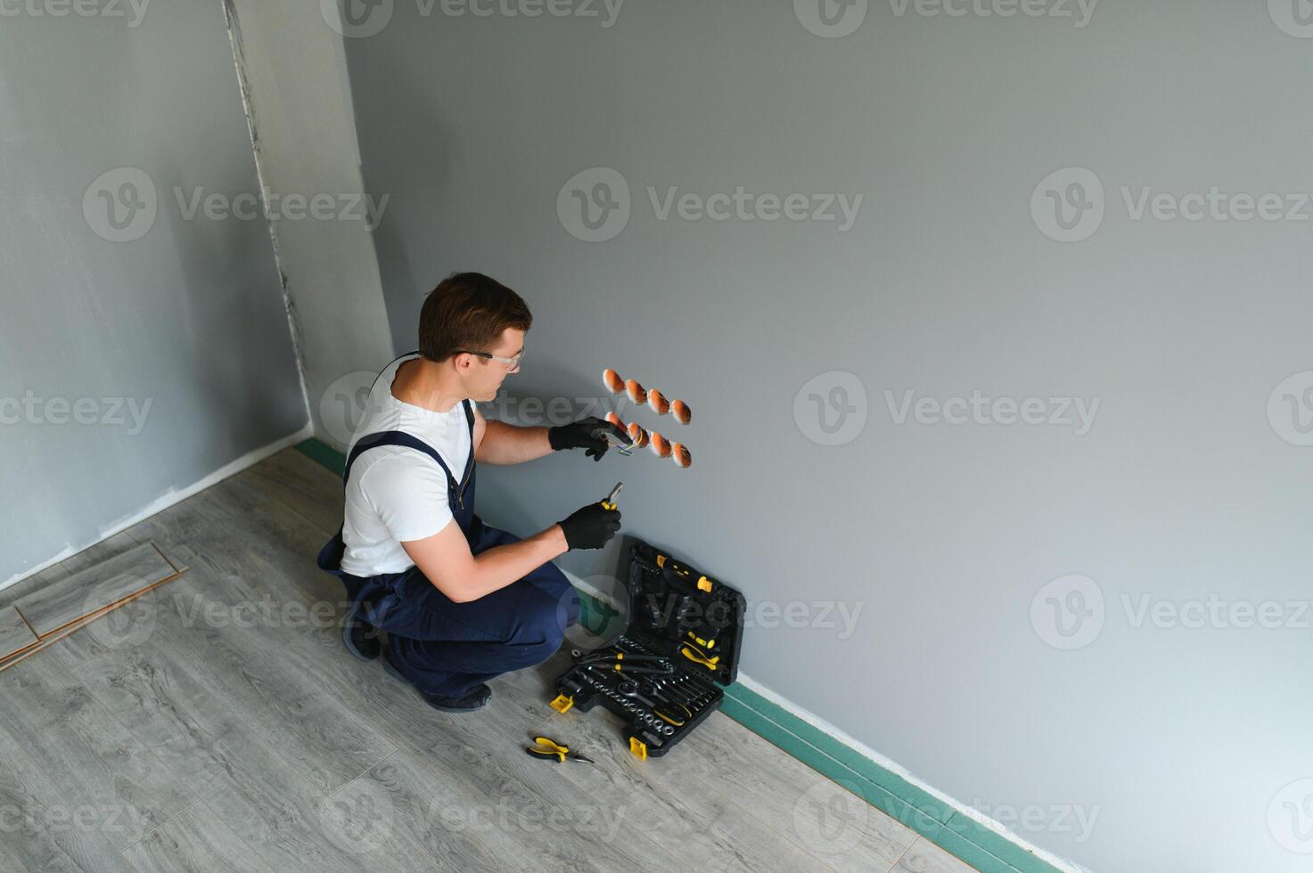Electrician in uniform mounting electric sockets on the white wall indoors photo