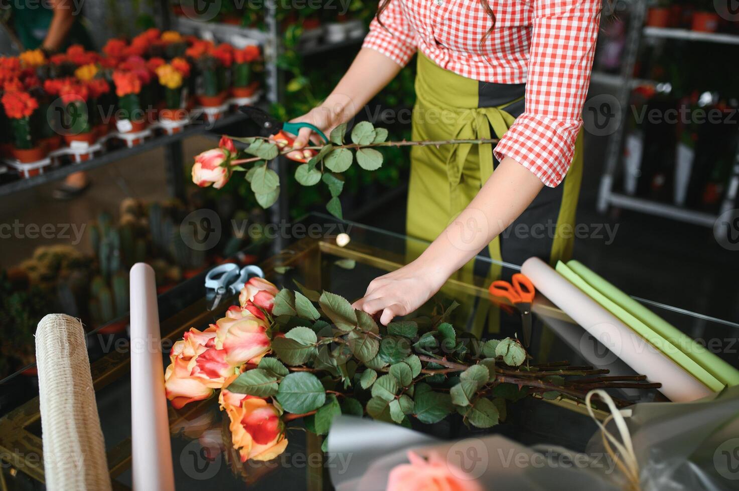 Cute girl florist collects a bouquet of roses in a flower shop. A beautiful florist creates a composition of flowers. Girl cuts flowers and removes stale leaves photo