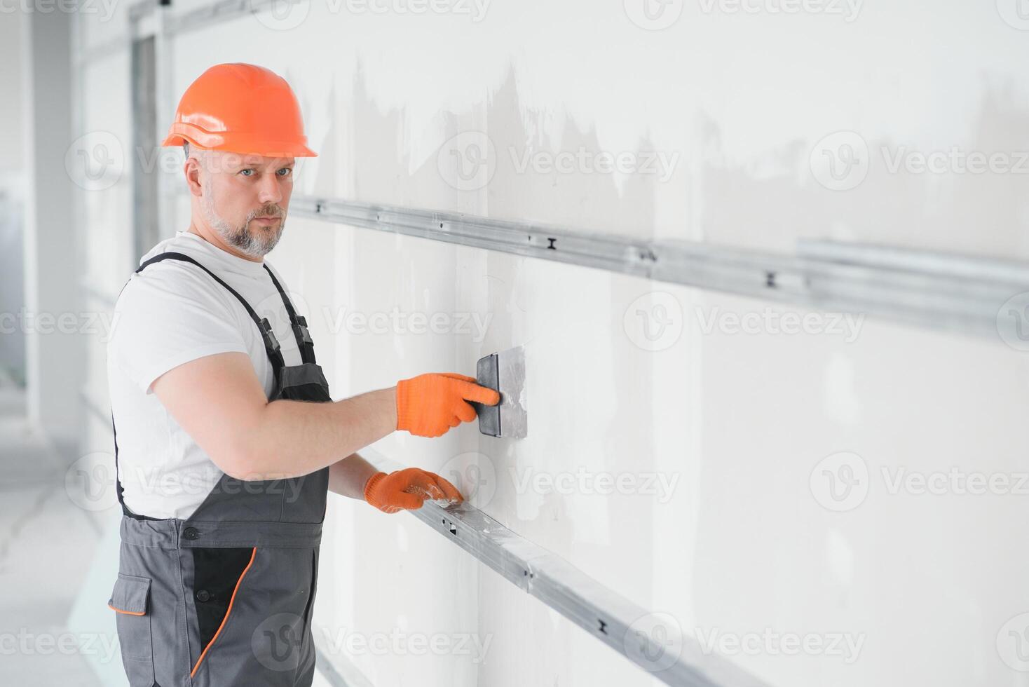 man drywall worker or plasterer putting mesh tape for plasterboard on a wall using a spatula and plaster. Wearing white hardhat, work gloves and safety glasses. Image with copy space. photo