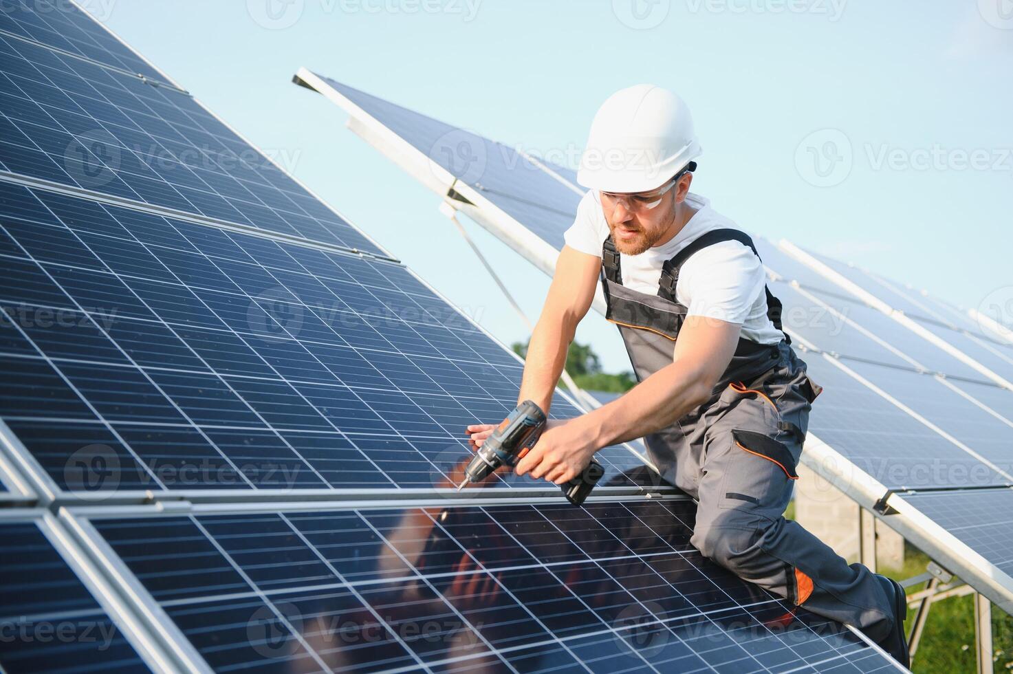 Side view of male worker installing solar modules and support structures of photovoltaic solar array. Electrician wearing safety helmet while working with solar panel. Concept of sun energy photo