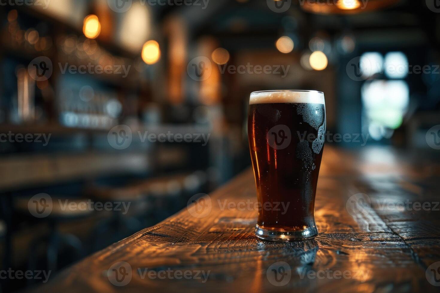 Glass of dark beer resting on a rustic wooden table, illuminated by soft ambient lighting in the cozy interior of a classic tavern photo