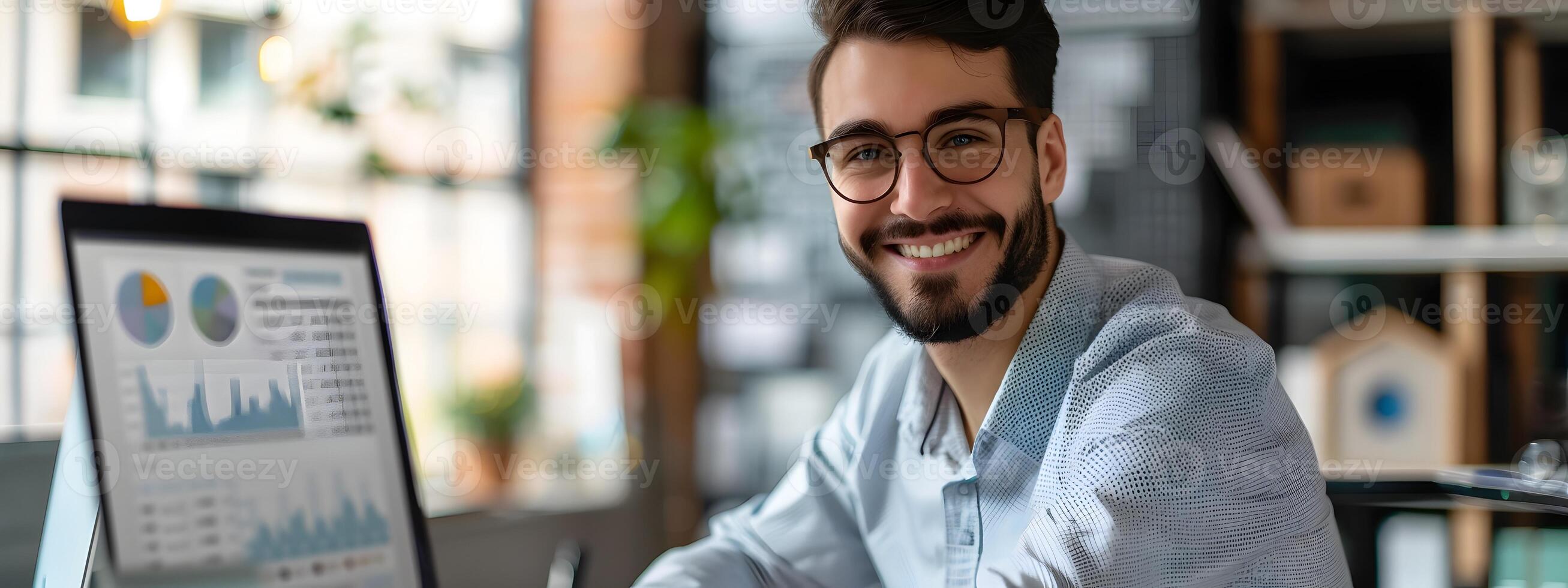 Smiling Young Male Business Analyst Reviewing Market Data Charts on Computer in Office photo