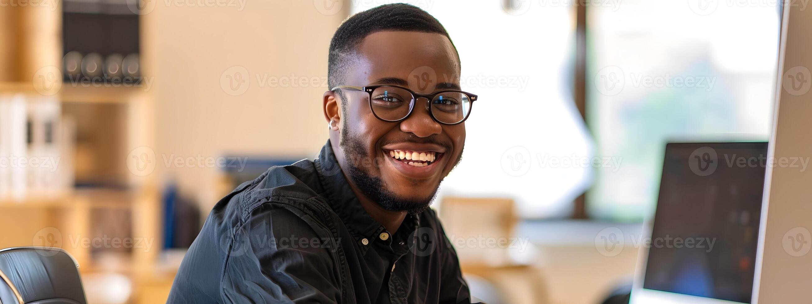 Smiling African American Program Administrator Happily Using Laptop in Modern Office Setting photo
