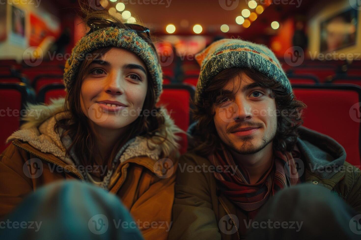 Young couple shares a special moment in a movie theater, smiling with anticipation, surrounded by red seats in warm, ambient light before the film starts photo