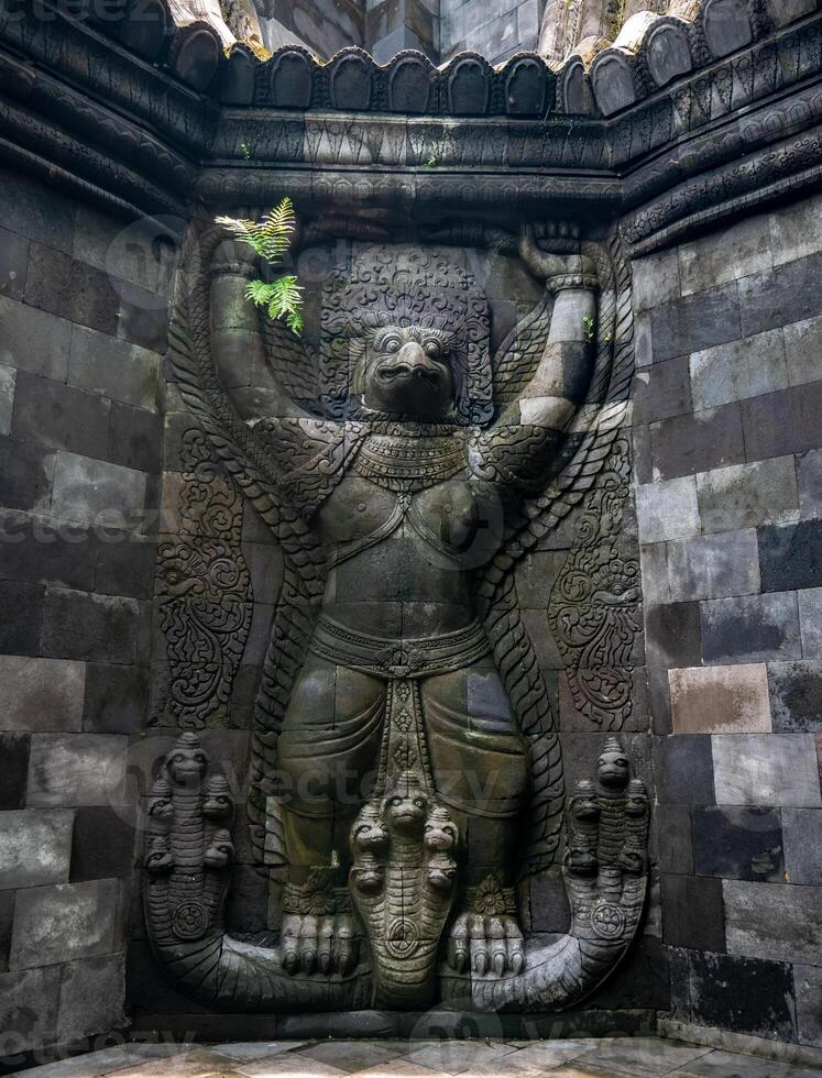A carved statue of Garudeya or Garuda clutching a multi-headed snake, located in an old temple complex in Java photo
