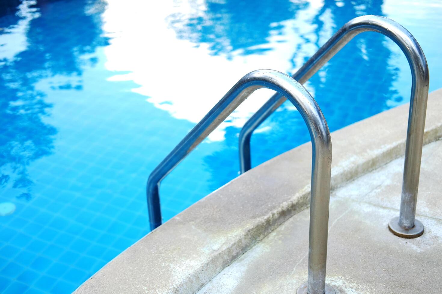Stainless steel handrail in blue water and ceramic tiles in swimming pool outdoor in garden of resort and hotel photo