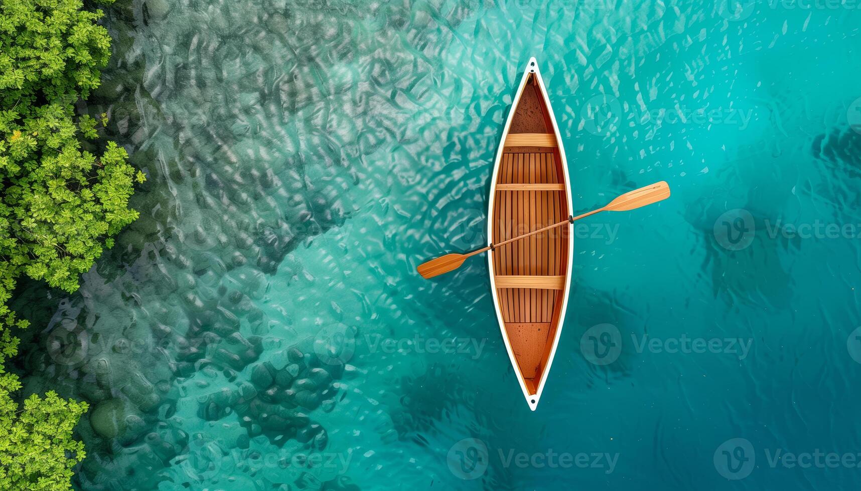Aerial view of a wooden canoe floating on crystal-clear turquoise water near green foliage, showcasing serene nature and tranquility. photo