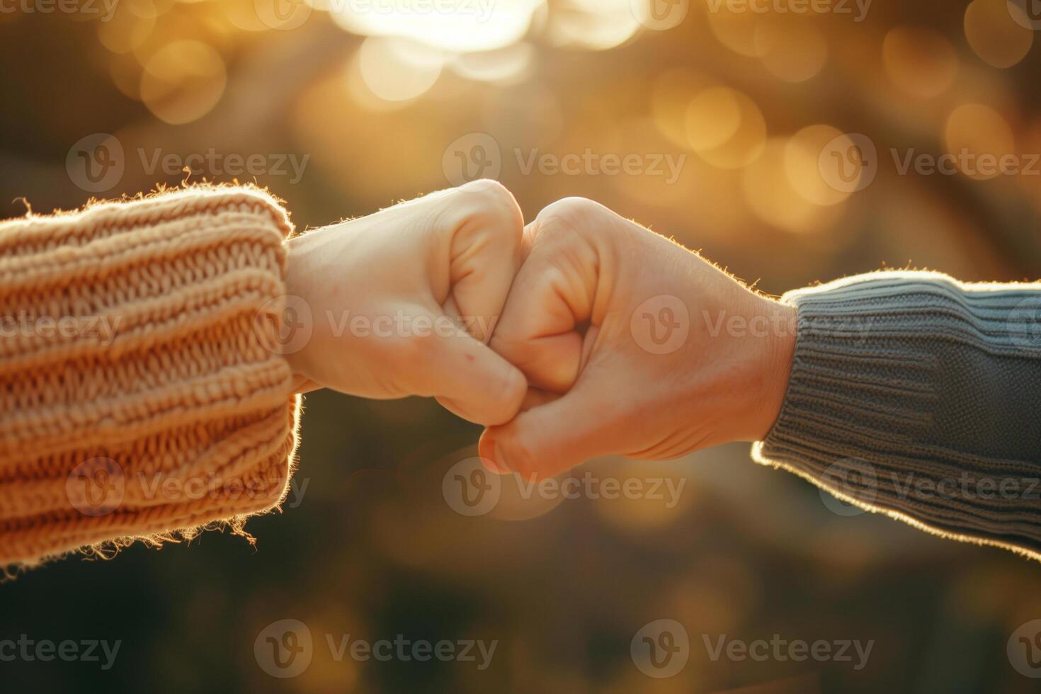Close-up of two people fist bumping outdoors with warm, golden light in the background, symbolizing friendship and teamwork. photo