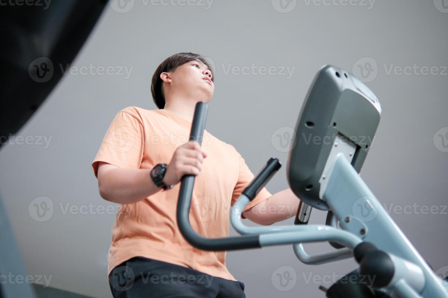Overweight man exercising on an elliptical machine in the gym photo