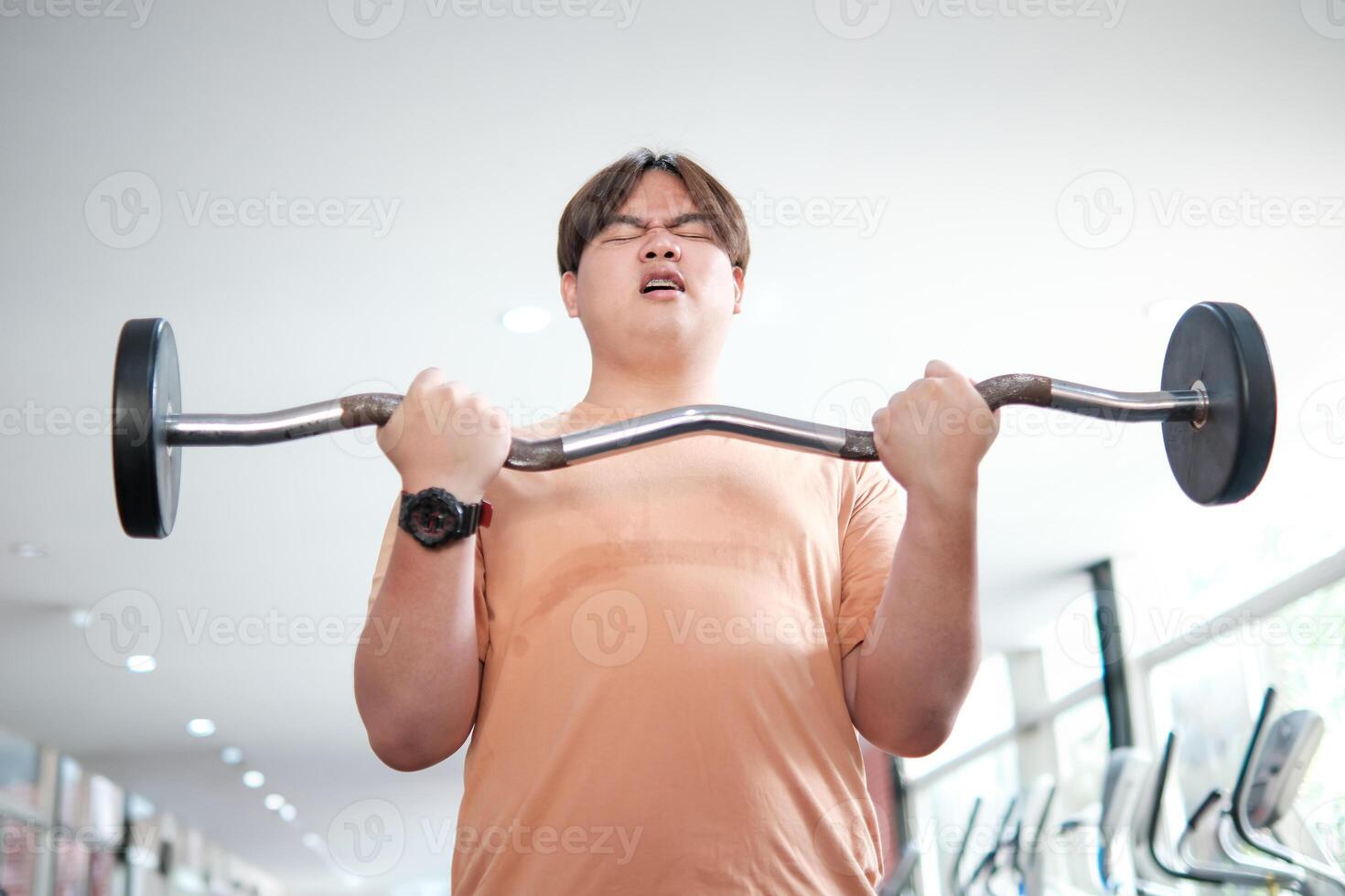 Overweight man lifting barbell with effort photo
