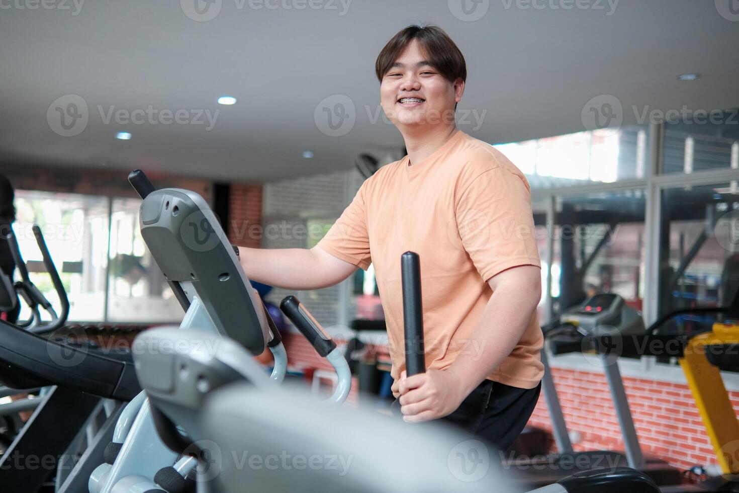 Overweight man smiling while exercising on elliptical photo