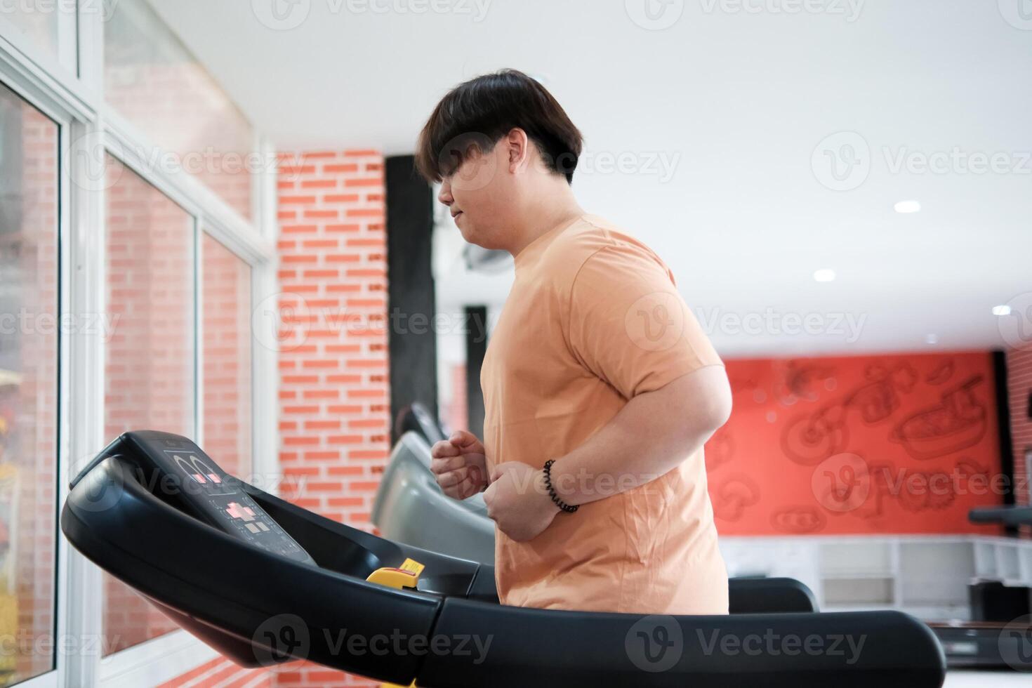 Overweight man running on treadmill in gym photo