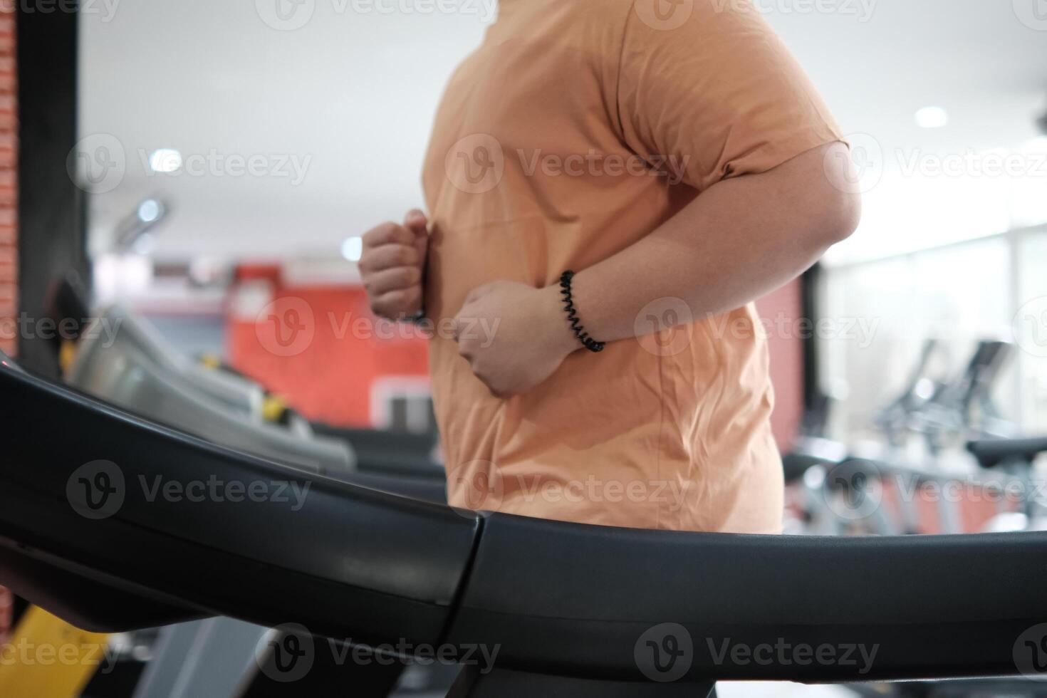 Overweight man running on treadmill in gym photo