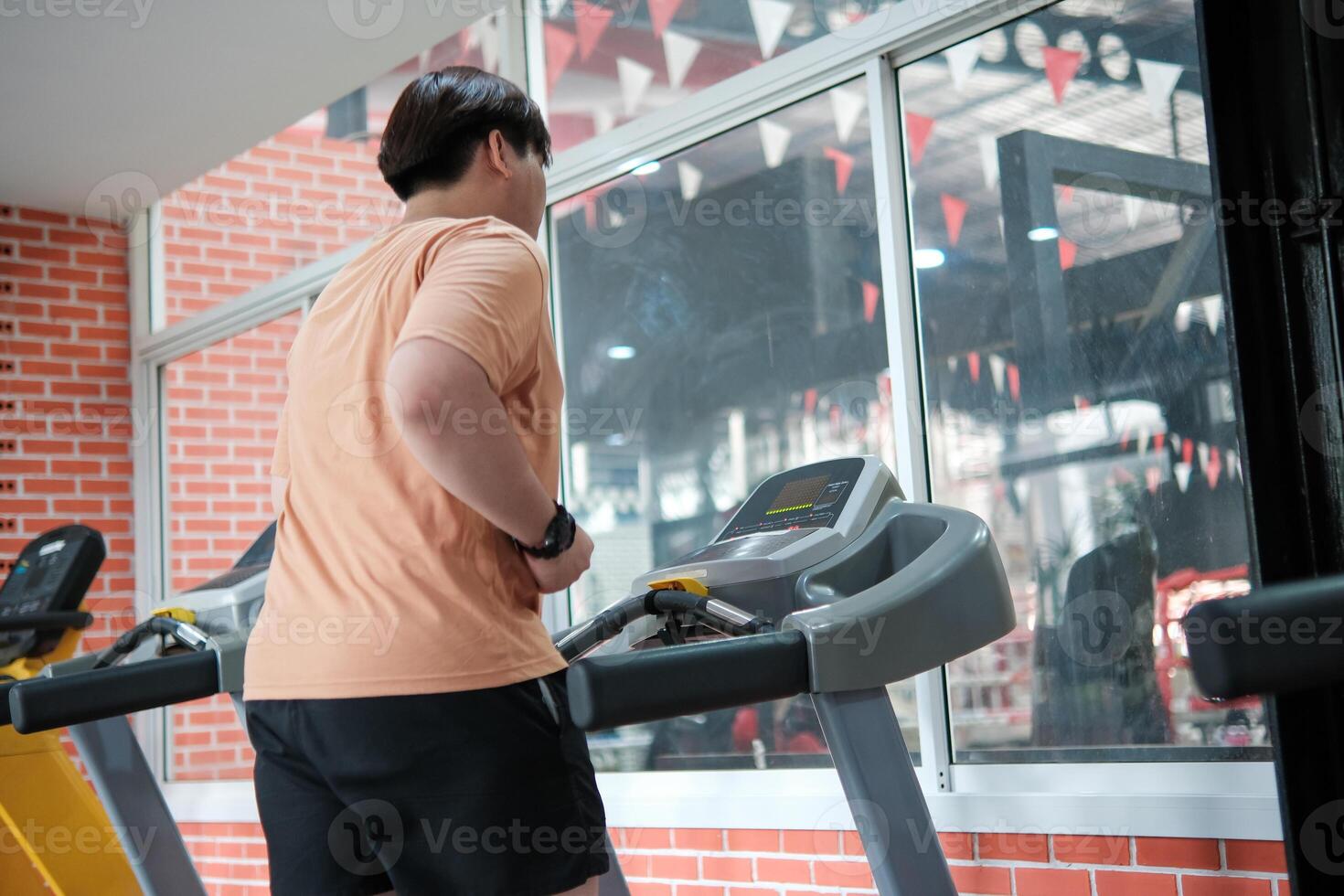 Overweight man running on treadmill in gym photo