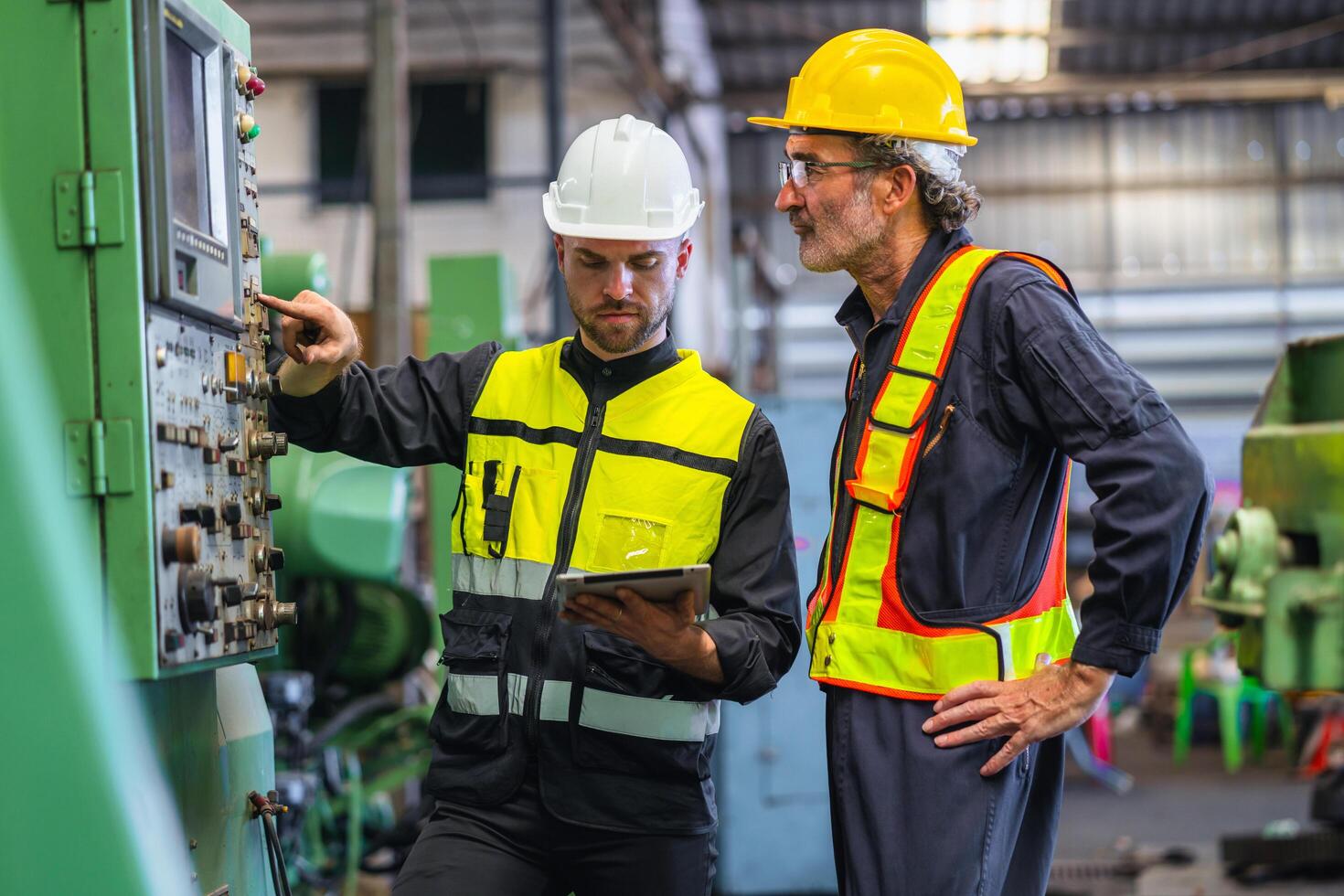 wo men in safety gear are standing next to a machine, one pointing at a button photo