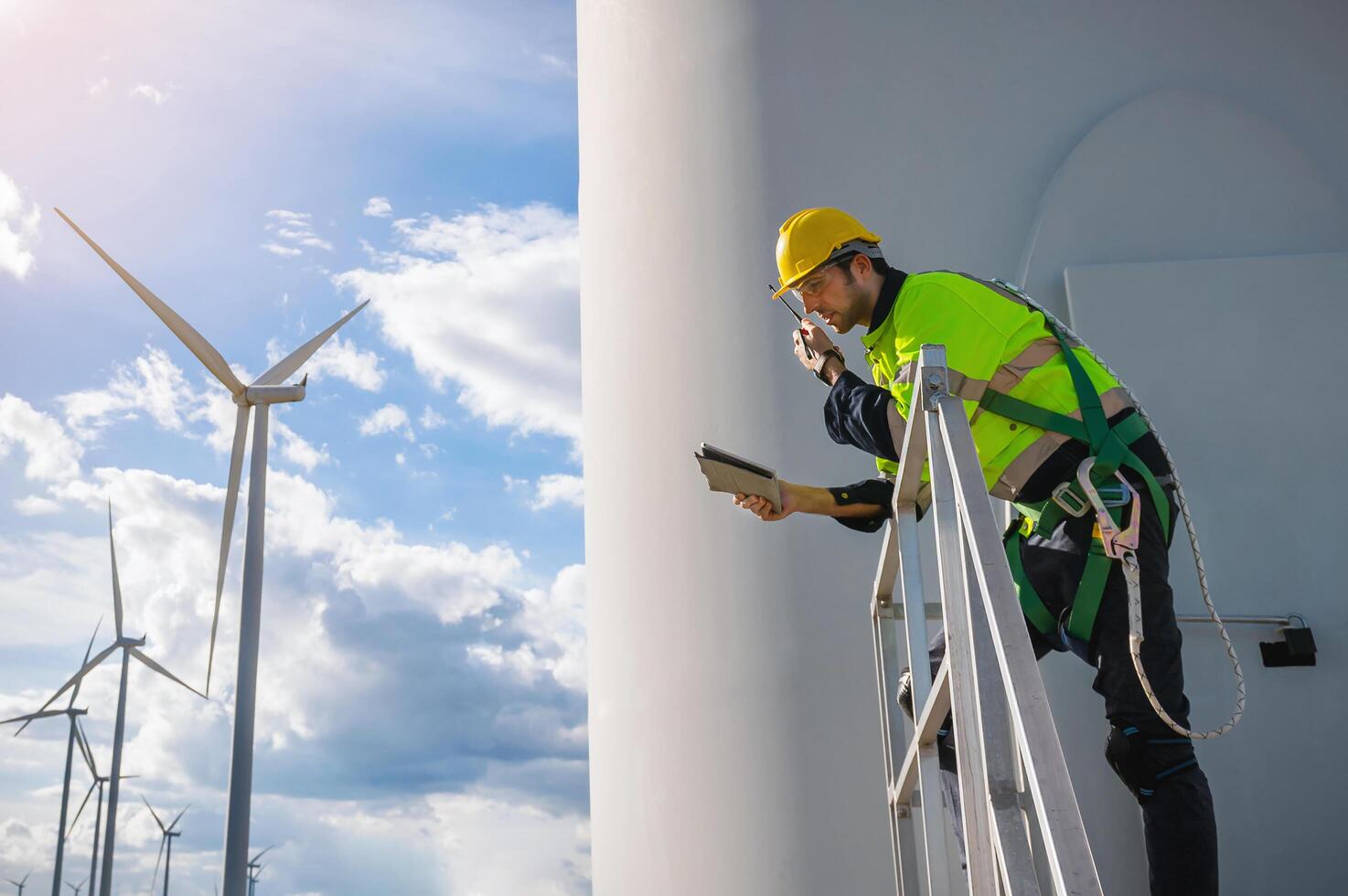 man in a safety vest is on a ladder next to a wind turbine photo