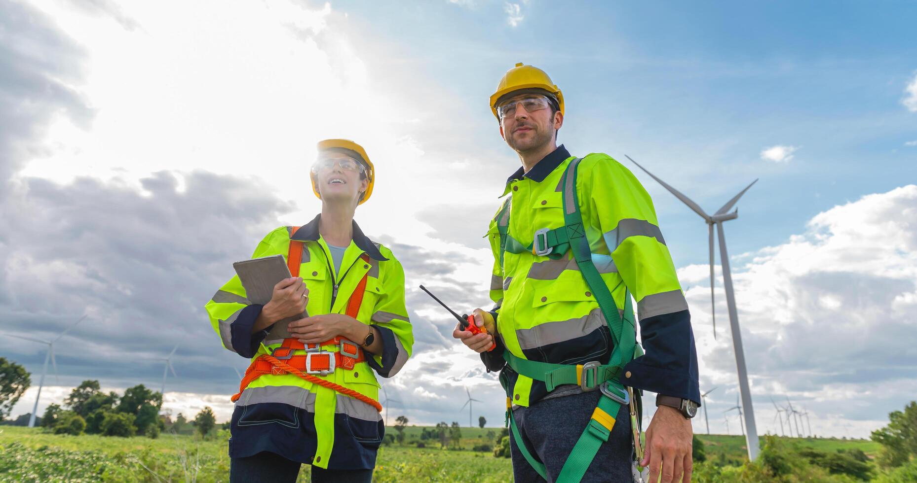 Two workers in safety gear are standing next to a wind turbine photo