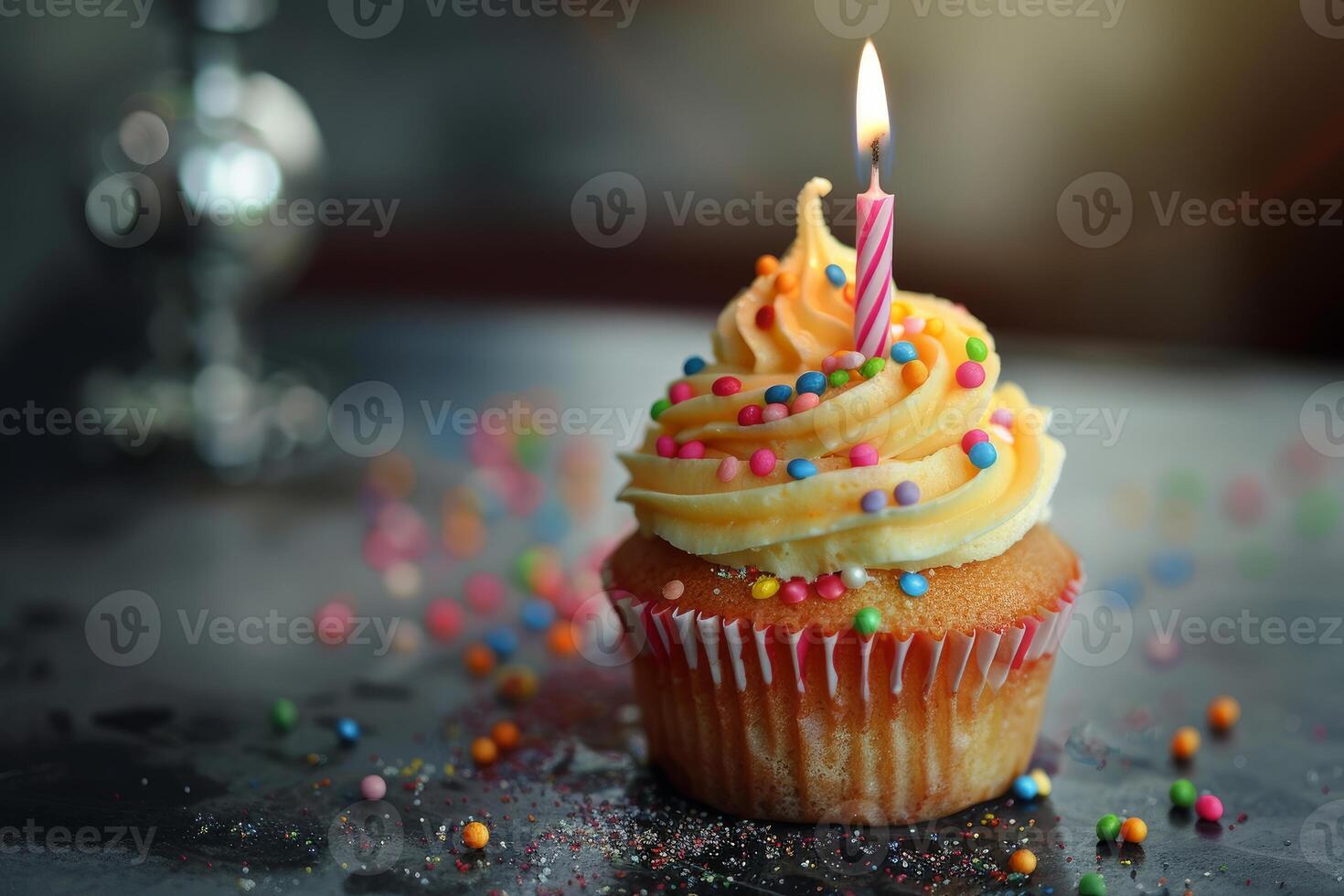 Delicious cupcake decorated with icing and sprinkles is sitting on table and lit candle is burning for birthday celebration photo