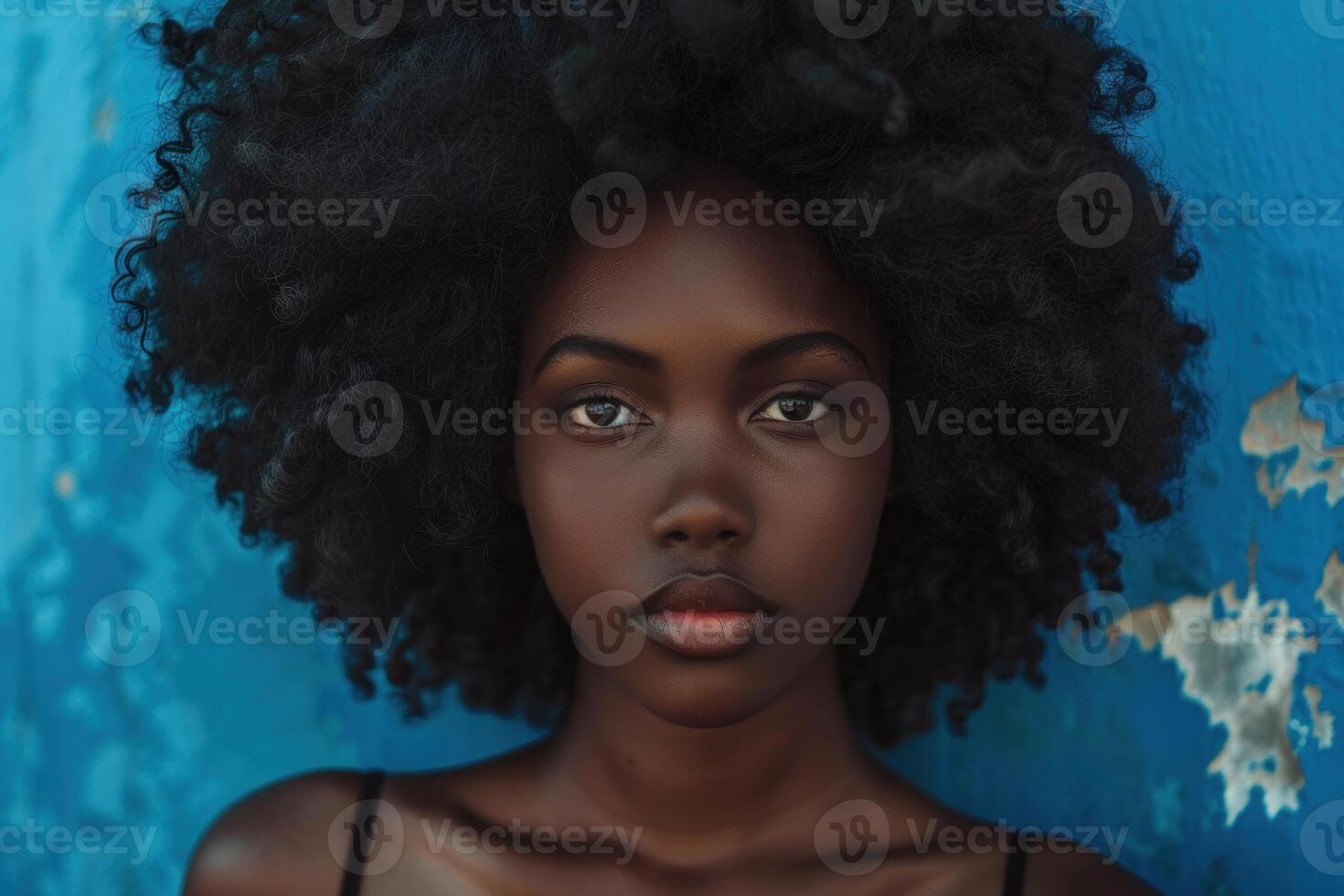 Beautiful black woman with afro hairstyle posing in front of blue wall photo