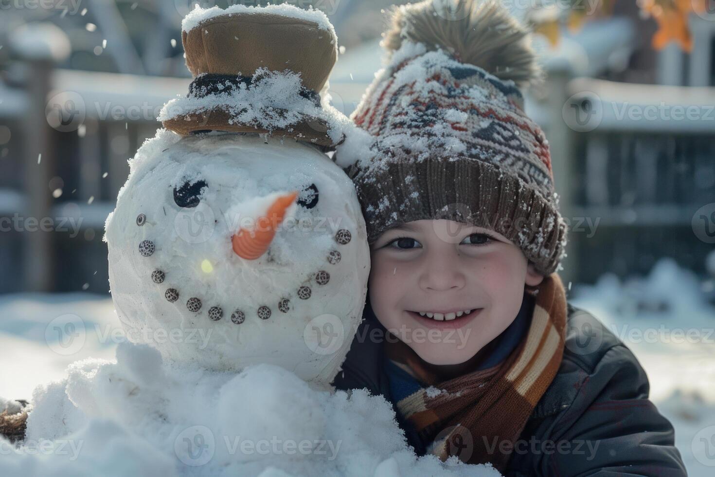 Smiling boy wearing knit hat and scarf lying in snow with snowman photo