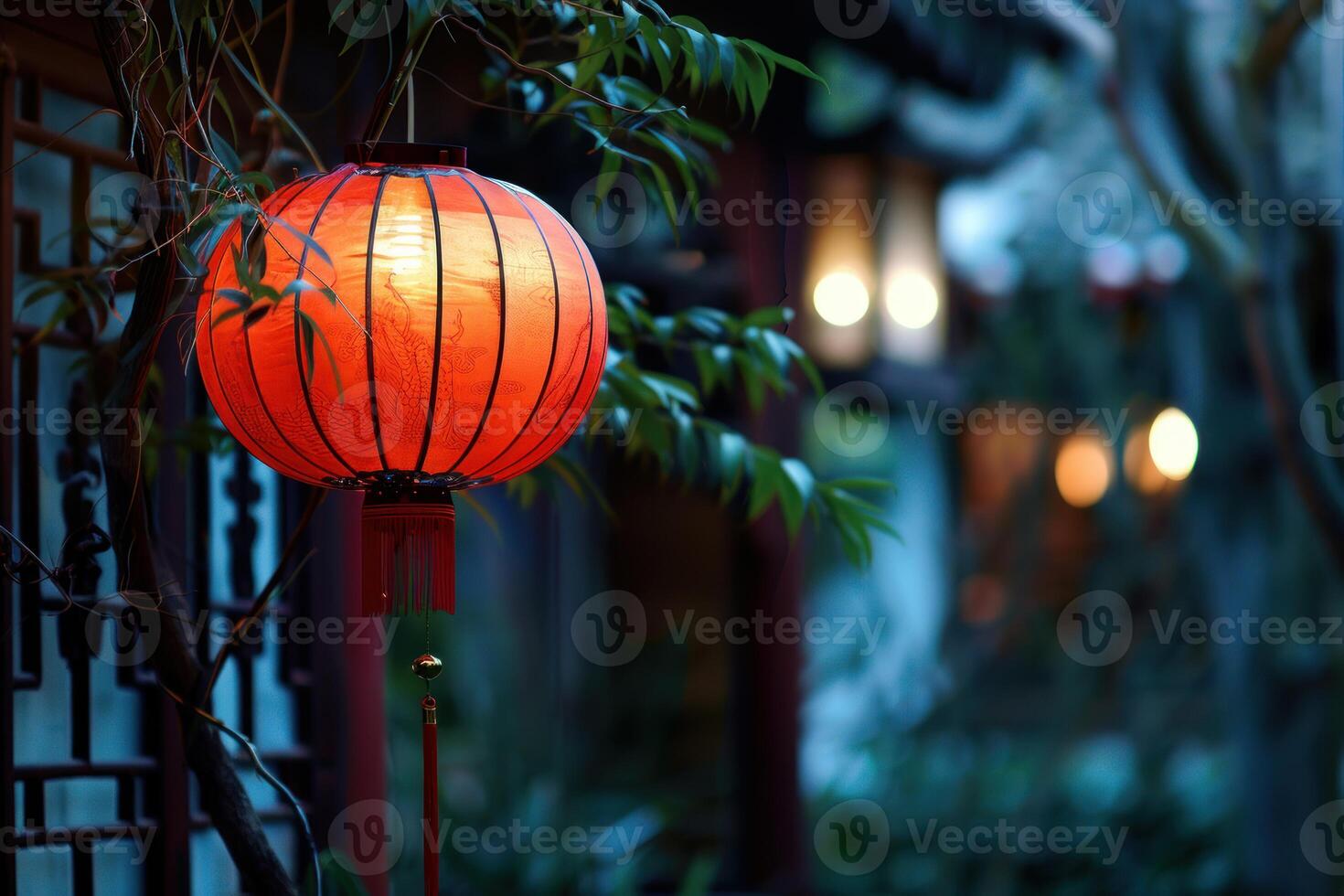Red chinese paper lantern hanging from tree branch illuminating traditional building photo