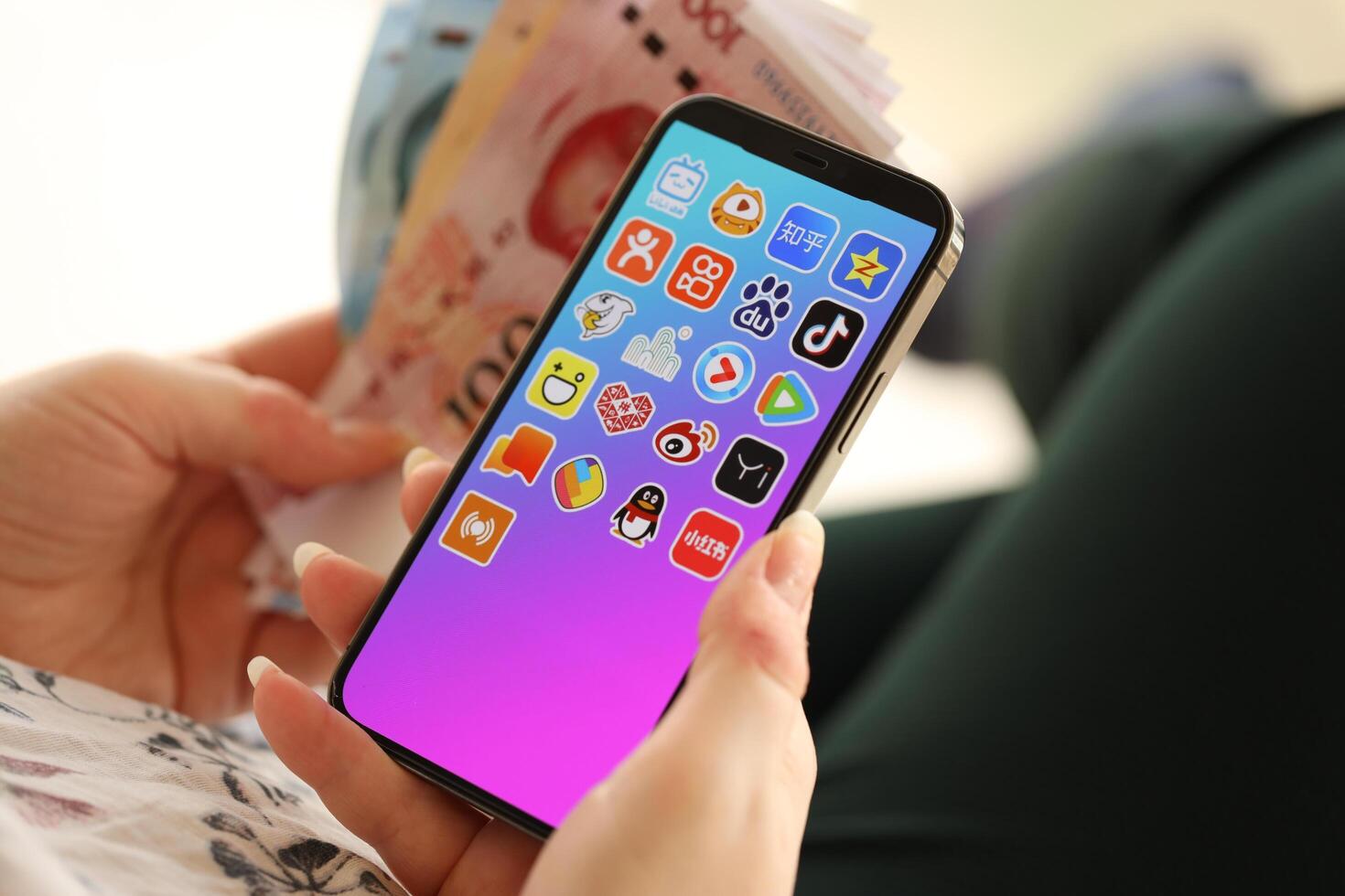 KYIV, UKRAINE - APRIL 1, 2024 Asian apps icon on smartphone screen and money in female hand photo