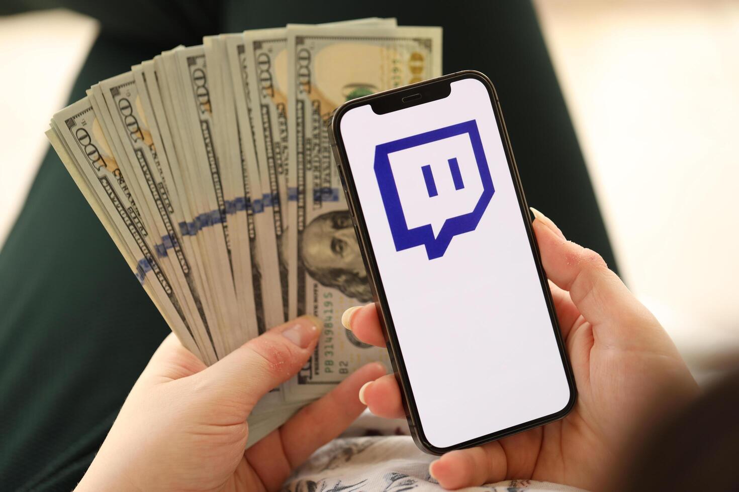 KYIV, UKRAINE - APRIL 1, 2024 Twitch icon on smartphone screen and money in female hand photo