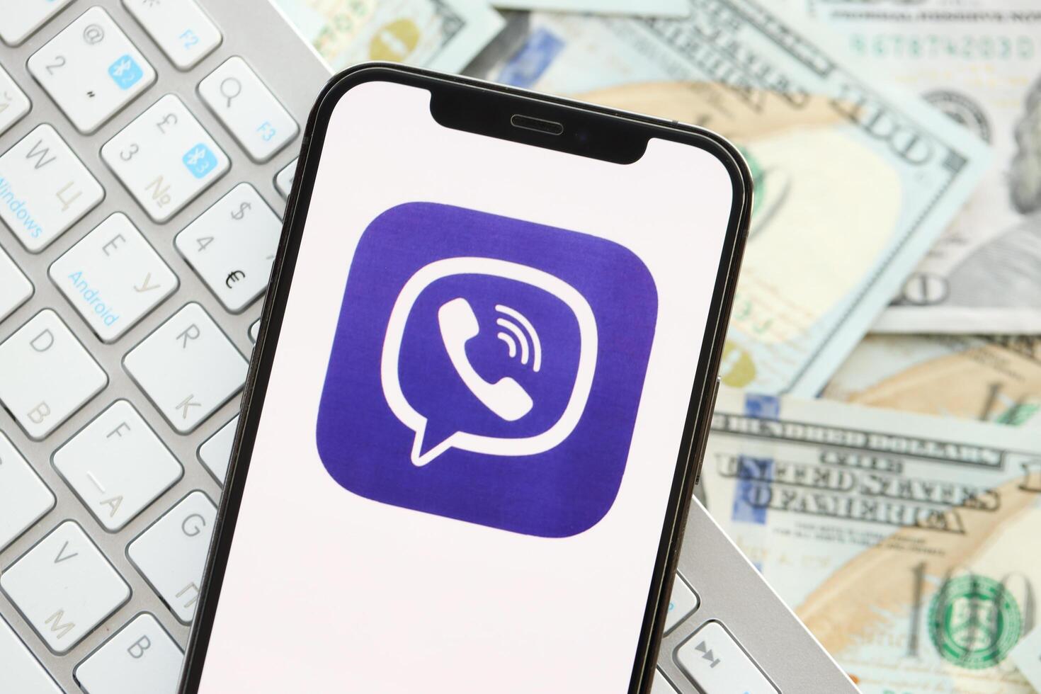 KYIV, UKRAINE - APRIL 1, 2024 Viber messenger icon on smartphone screen on many usd money bills photo