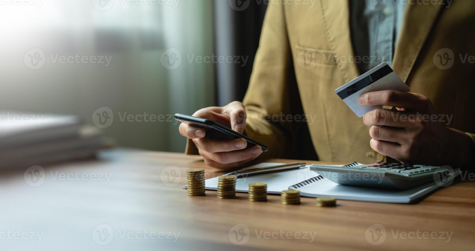 Man Managing Finances with Credit Card and Smartphone at Office, Calculating Expenses and Savings with Stacked Coins and Calculator, Using Modern Technology for Digital Payments and Online Banking photo