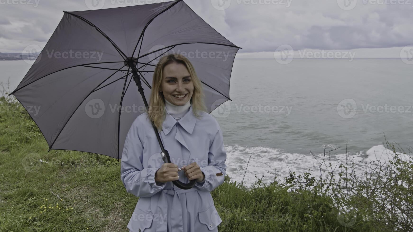 Tender woman with umbrella closing her boyfriend eyes with her hand at the sea shore. Stock clip. Cold windy weather at the sea coast. photo