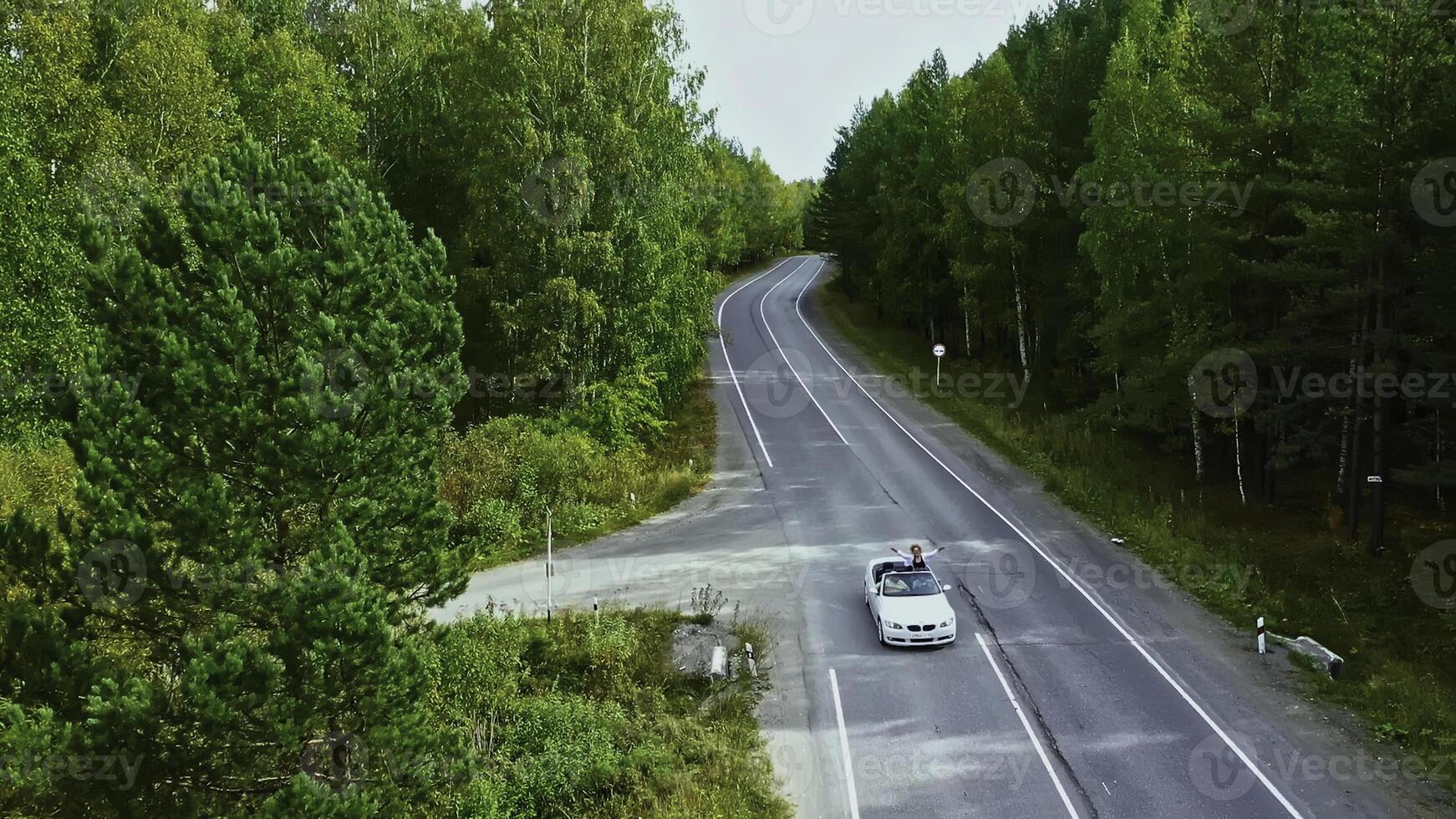 Flying over the rural road and driving cabriolet car. Footage. Traveling in the countryside through the green forest. photo
