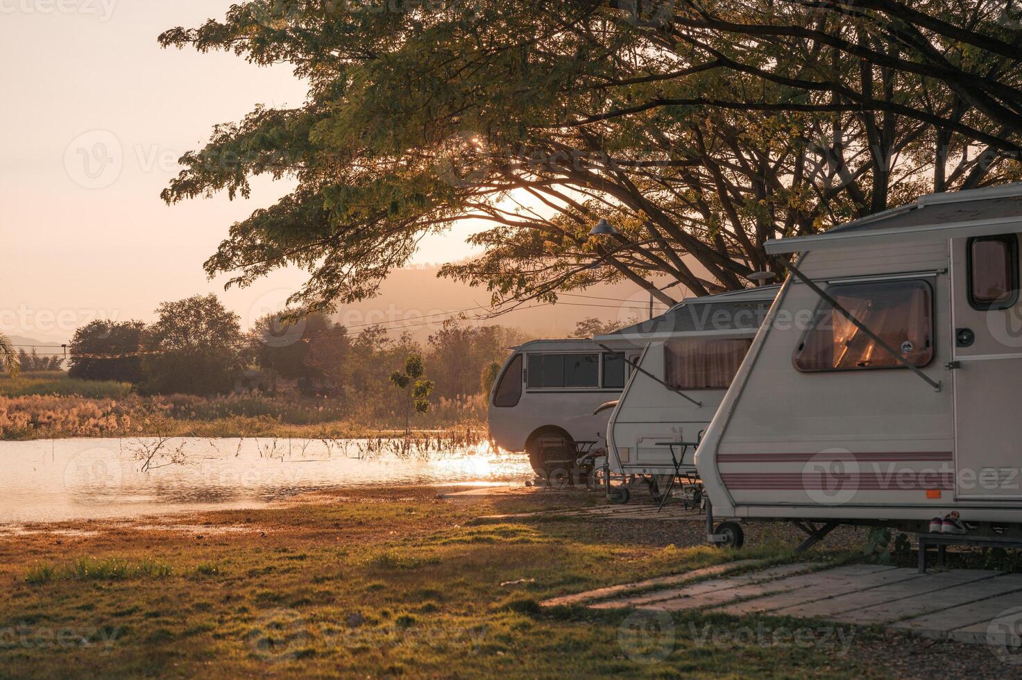 Motor home under big tree on campground by the lake in the evening photo