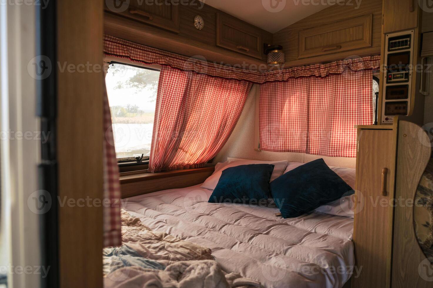 Inside of camper van with bed, pillow, curtain on window at campsite photo