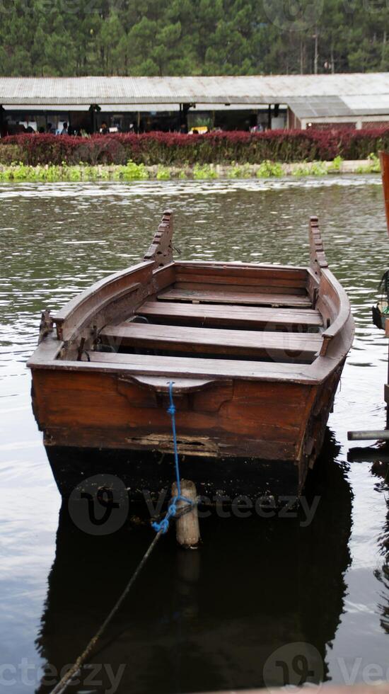 Wooden Boat Moored on Calm Lake with Reflections and Scenic Forest Background in Peaceful Outdoor Setting photo