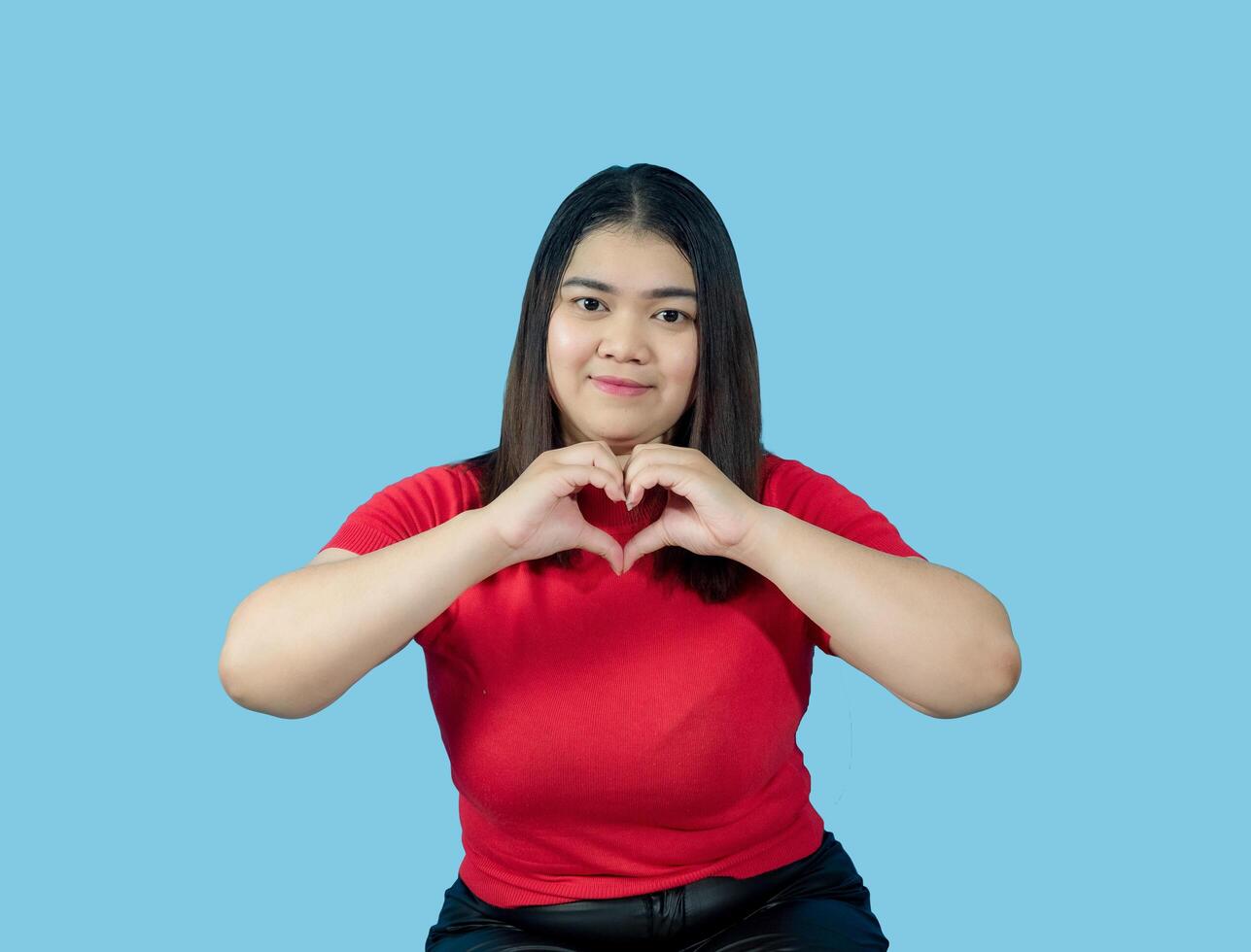 Portrait girl young woman asian chubby fat cute beautiful pretty one person wearing a red shirt is sitting, looking smiling happily holding copyspace imaginary on the isolated blue color background photo