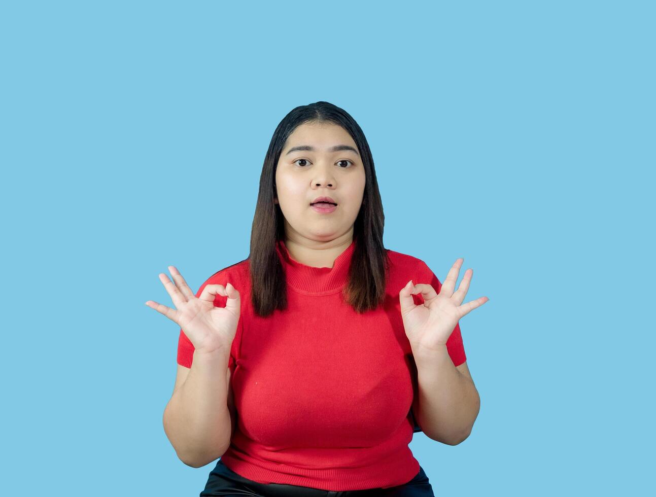 Portrait girl young woman asian chubby fat cute beautiful pretty one person wearing a red shirt is sitting, looking smiling happily holding copyspace imaginary on the isolated blue color background photo
