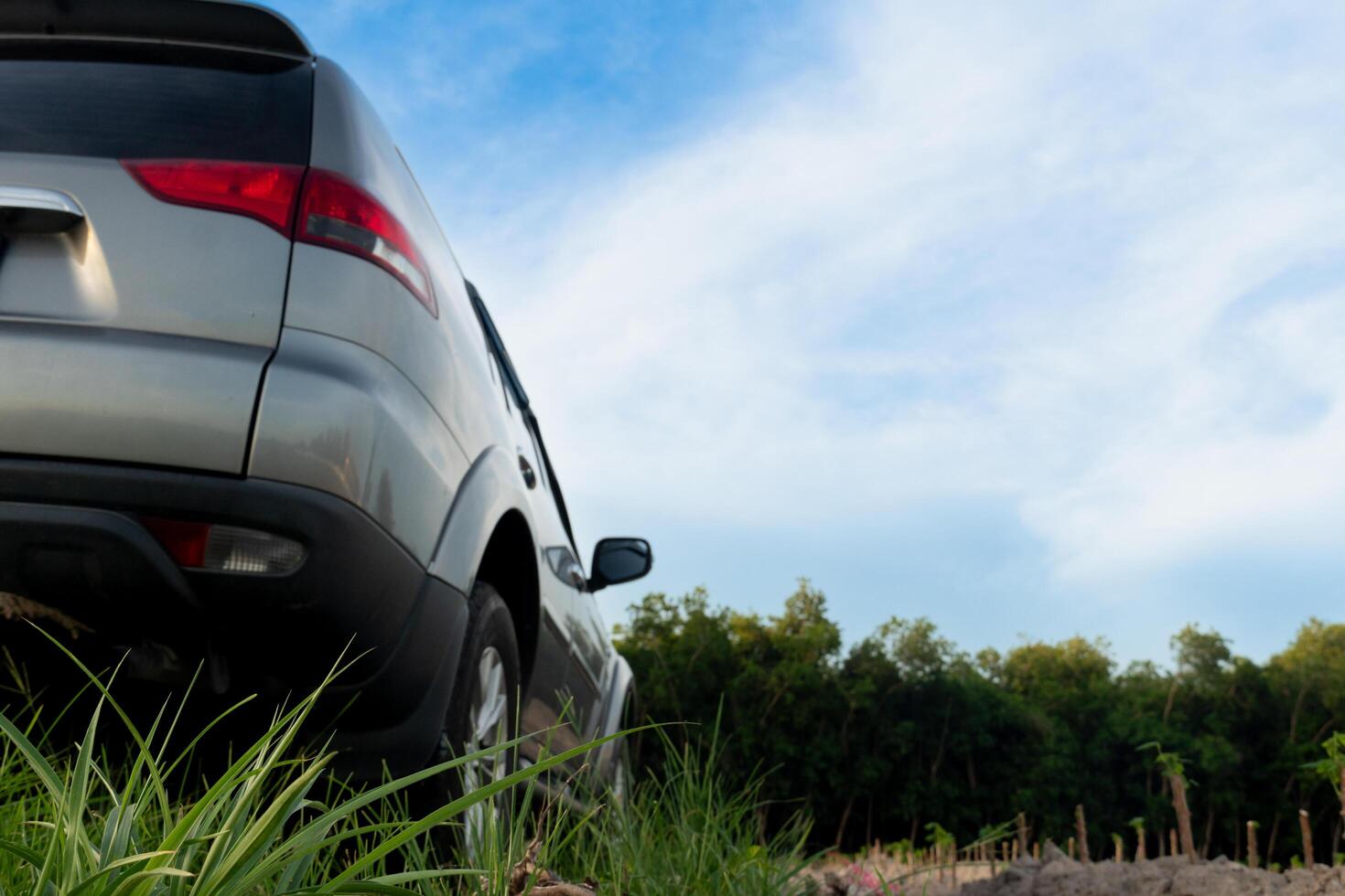 Beside view of grey car parking on the ground with green grass for front groung. Background of soil and dark forest under blue sky and white clouds. photo