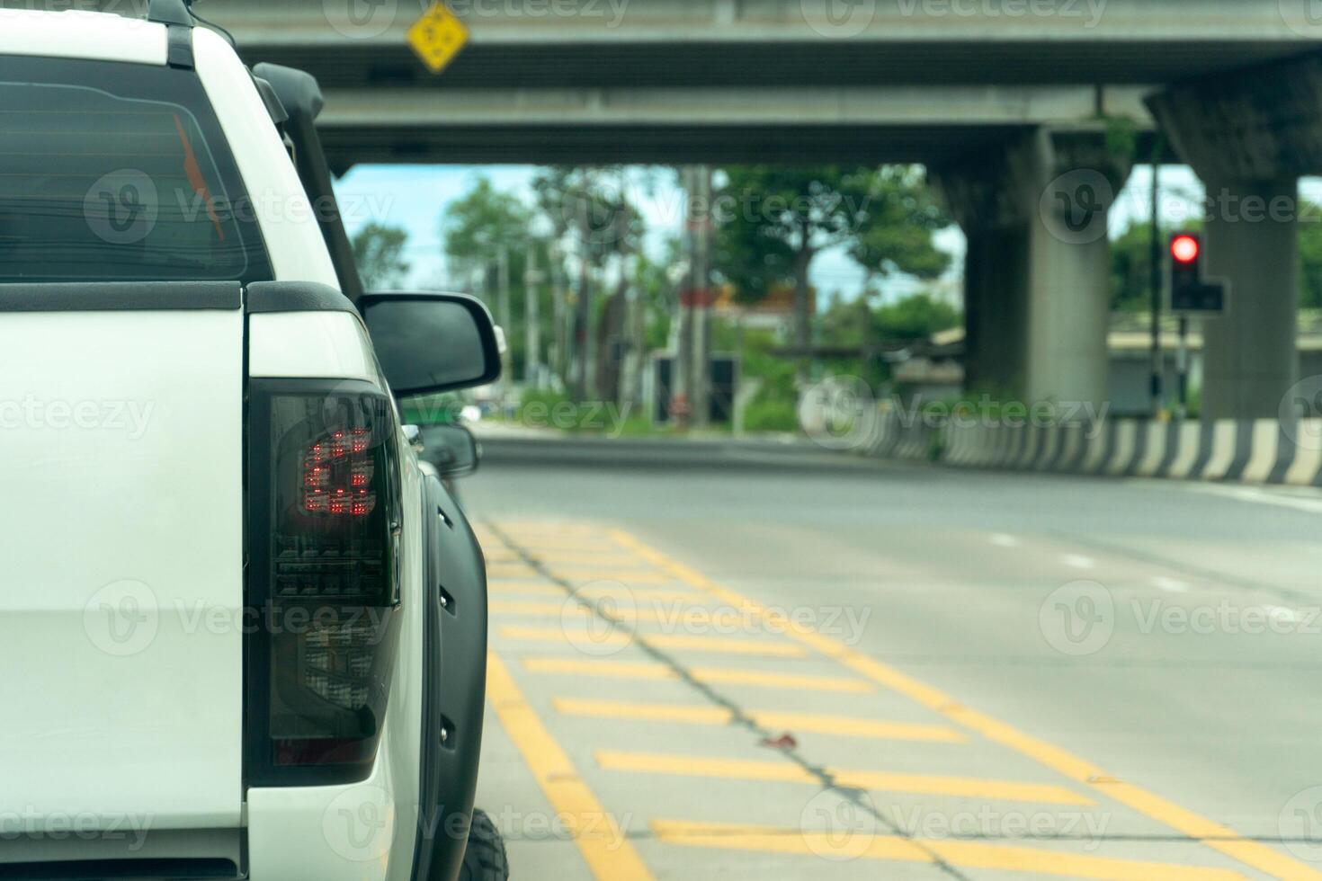 Rear side of white pickup car on the concrete road. With turn on brake light. background of traffic red light in the crossroads. under concrete bridge at Thailand. photo