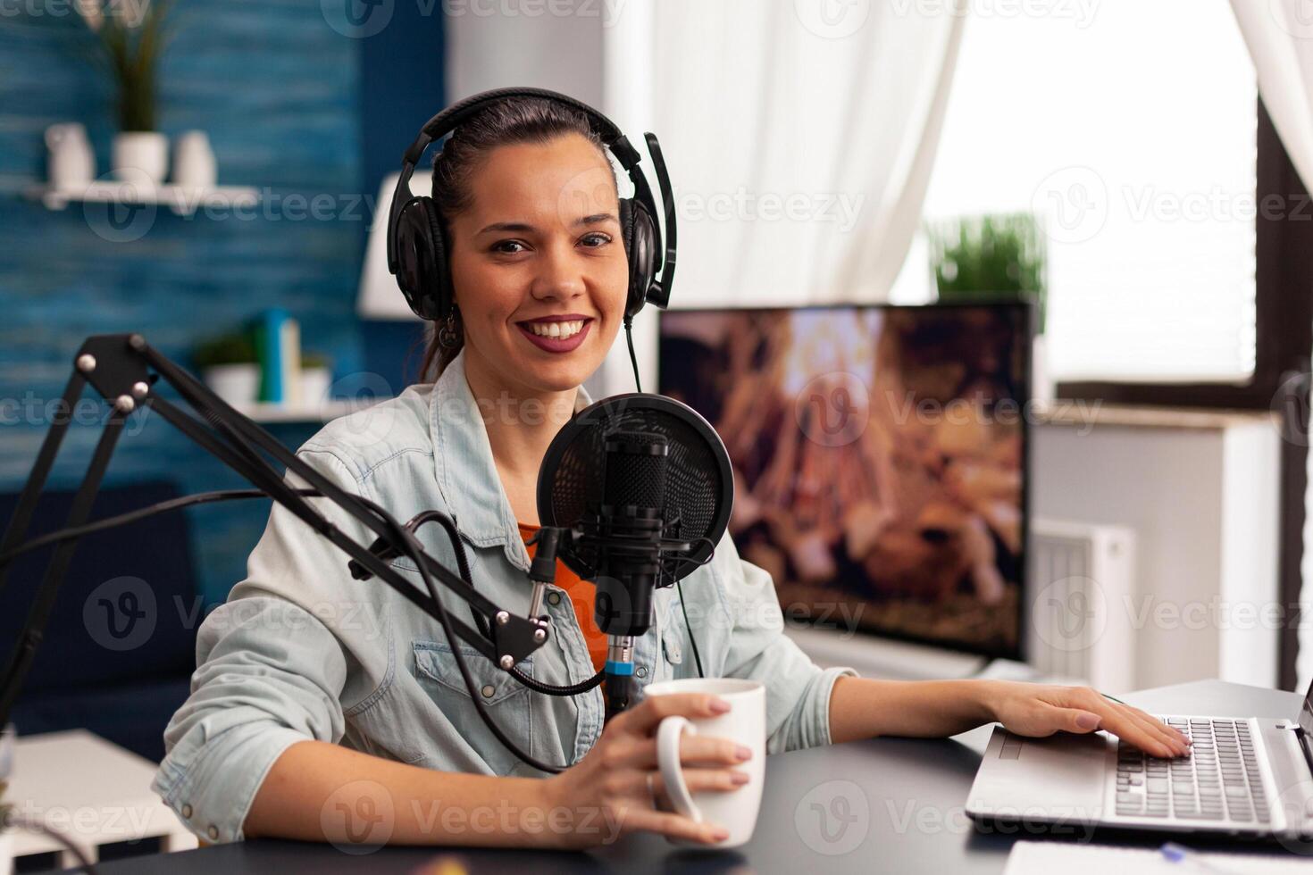 Smiling influencer woman sitting in front of camera recording for fashion blog. Digital blogger vlogger streaming talk show in studio using headphones, professional podcast microphone photo