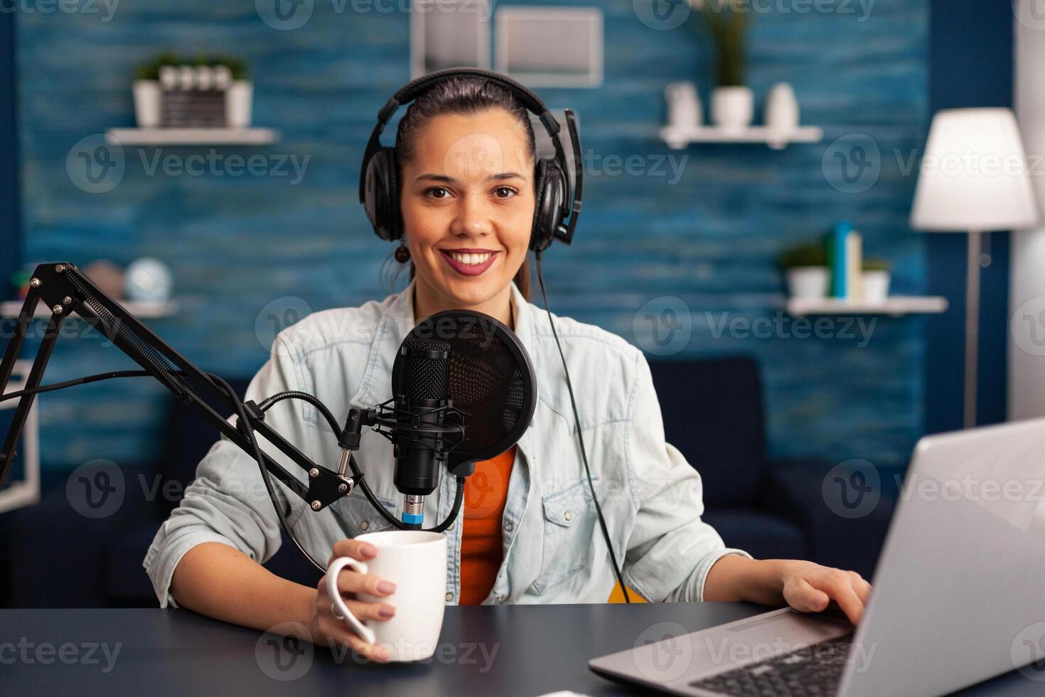 Portrait of smiling blogger looking at camera before starting live at home studio podcast holding cup of coffee. Content creator blogger woman recording brodcast live streaming for Internet photo