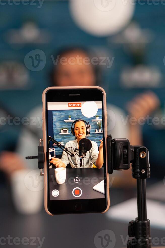 Close up of influencer vlogger record live broadcast looking at smartphone on tripod at home studio podcast. Creative content creator making online for subscribers audience photo