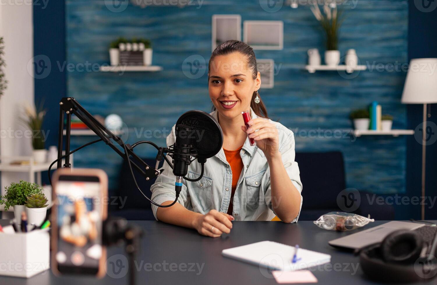 Famous blogger recording red lipstick review for beauty vlog. Woman vlogger making live make up tutorial share on social media using professional microphone looking at camera for digital podcast photo