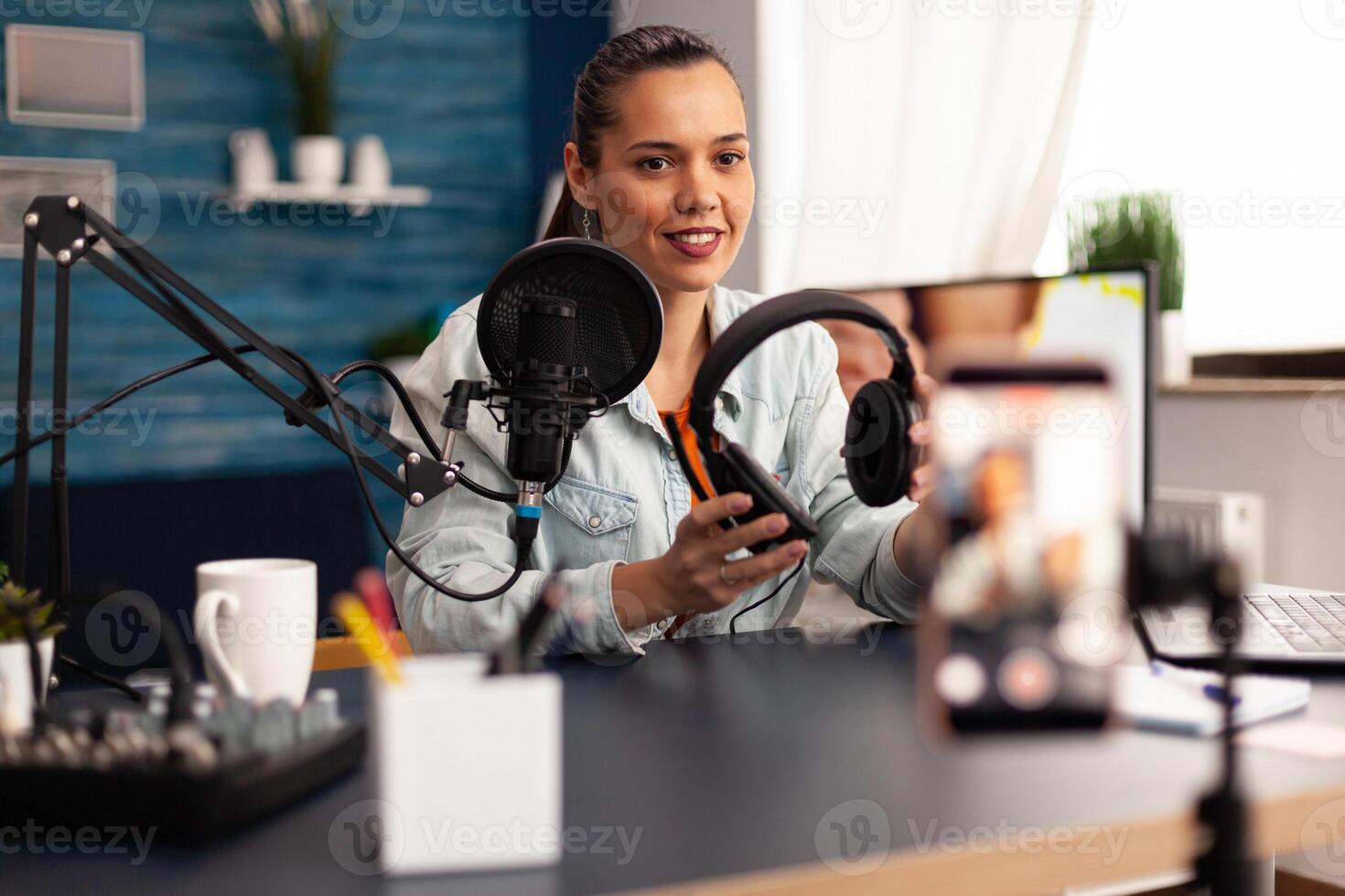 Influencer presenting headphones for giveaway to camera while making blog in home studio. Creative content creator influencer recording online internet web podcast gift for audience photo