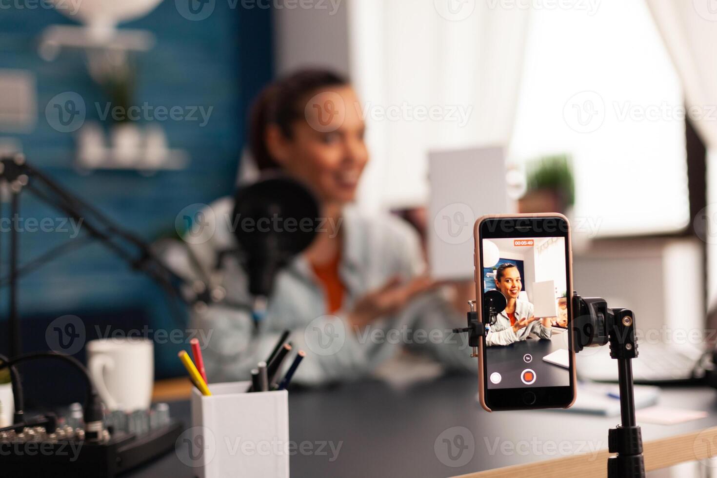 Influencer holding white gift box while recording videoblog for social media. Creative content creator making broadcast concept speaking and looking at smartphone on tripod at home studio podcast photo