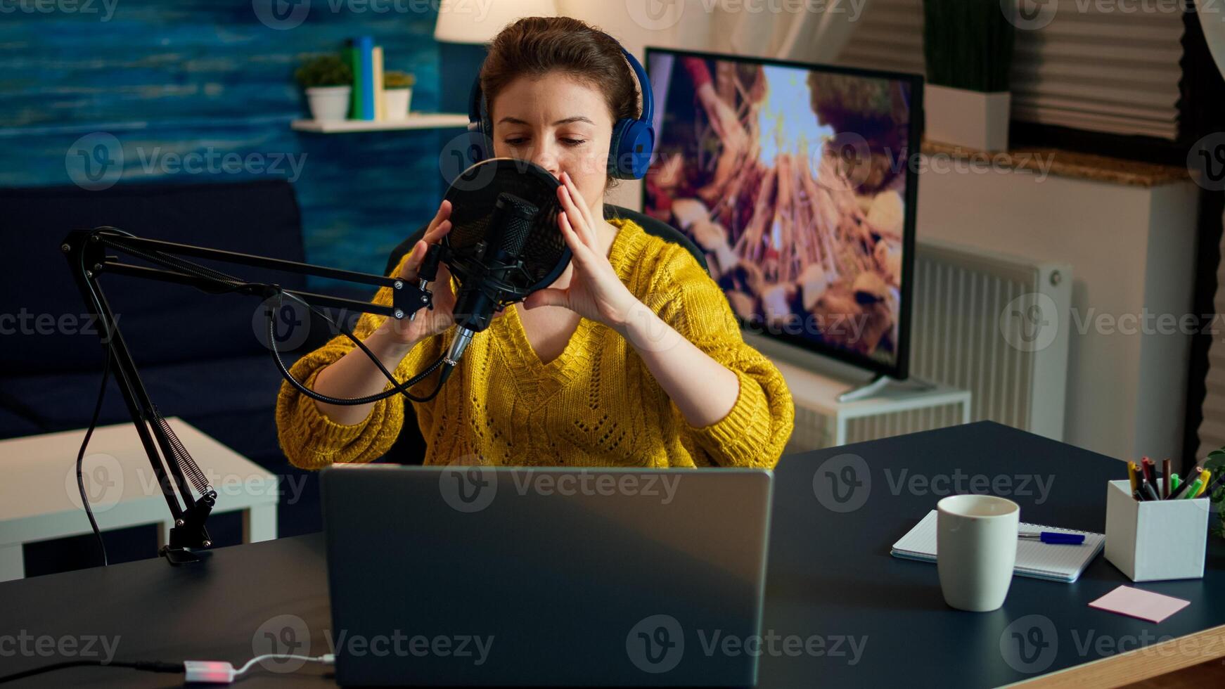 Creative influencer with headphones preparing to speak during live on social media recording vlog. On-air online production internet broadcast show host streaming podcast content from studio photo
