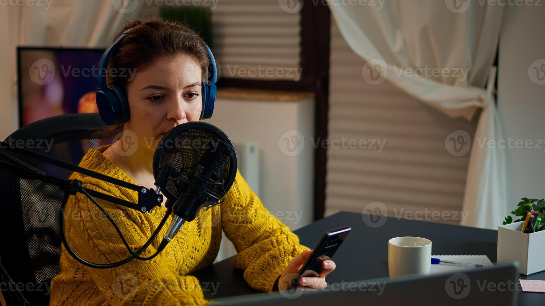 Internet show host answering at questions of fan texting on phone and talking at microphone from home podcast studio. Show production broadcast presenter streaming live content recording digital media photo