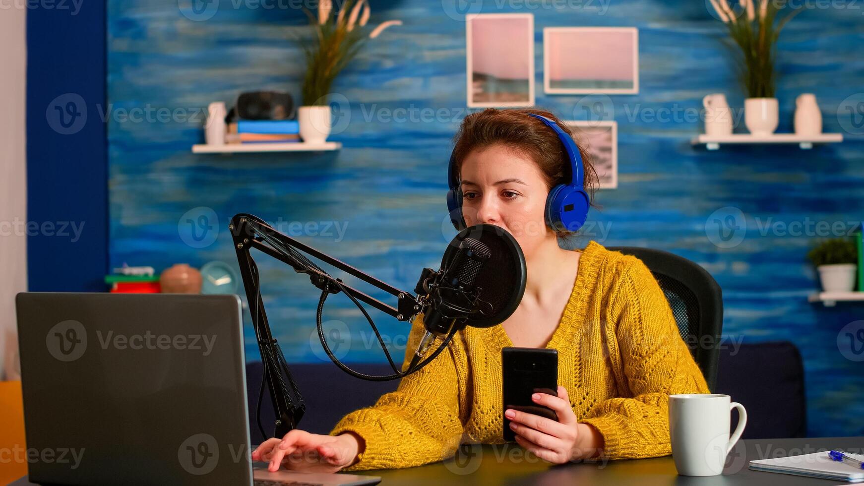 Blogger woman recording for her blog in home studio reading messages on smartphone. On-air online production internet broadcast show host streaming live content for social media photo