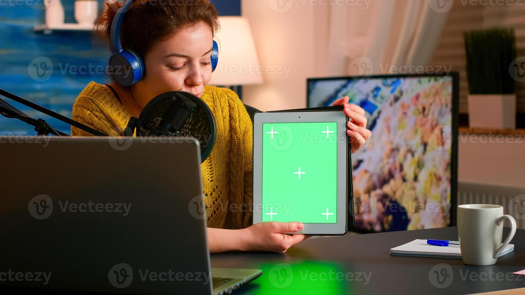 Influencer holding tablet with green screen and speaking into microphone during podcast in home studio. On-air production internet broadcast host streaming live content using chroma key mockup display photo