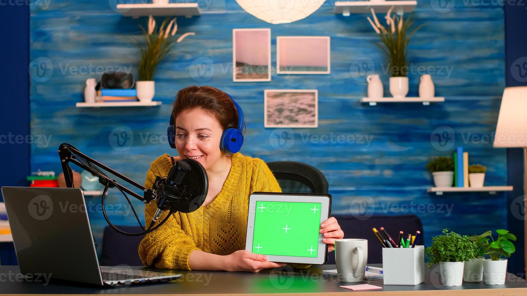 Vlogger looking at laptop and talking about tablet with chroma key desktop. On-air production internet broadcast host streaming live content using mochup, green screen, izolated desktop photo